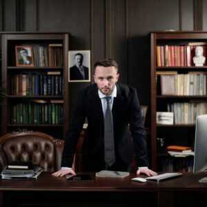 Confident businessman standing at desk with USA flag in office library.